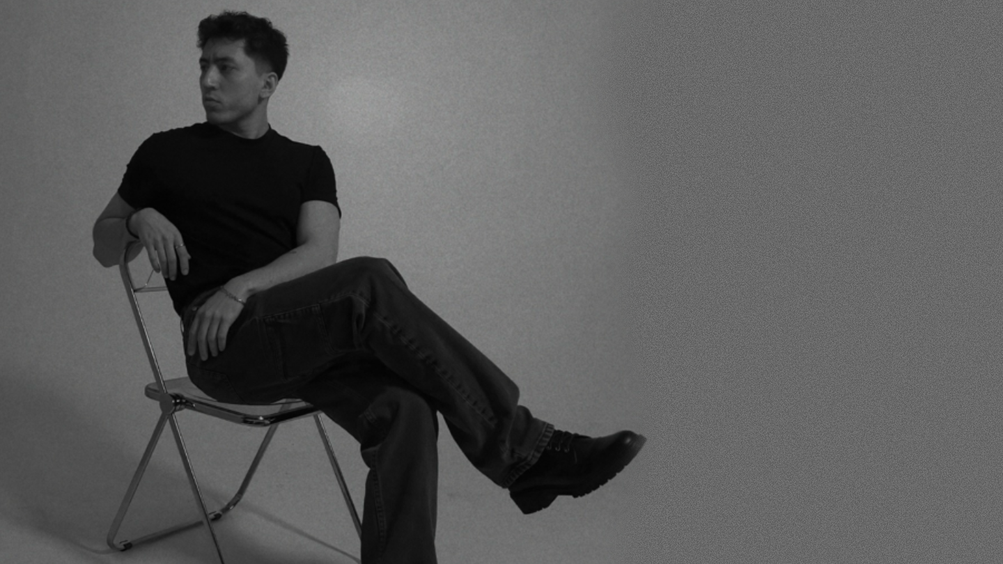 Efe Aydınalp, Computer Engineering student and visual practitioner, seated on a folding chair in a black-and-white studio portrait