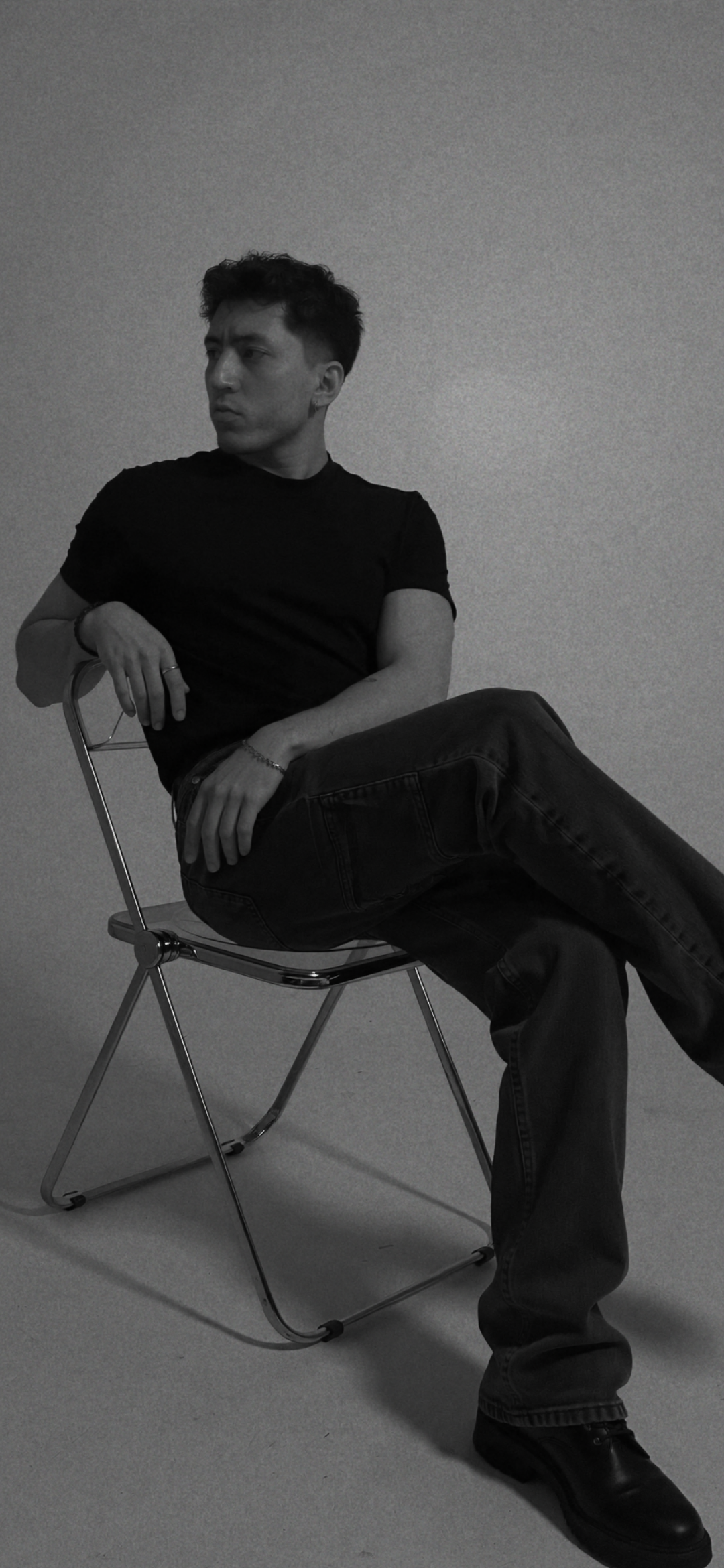 Black-and-white studio portrait of Efe Aydinalp seated on a folding chair